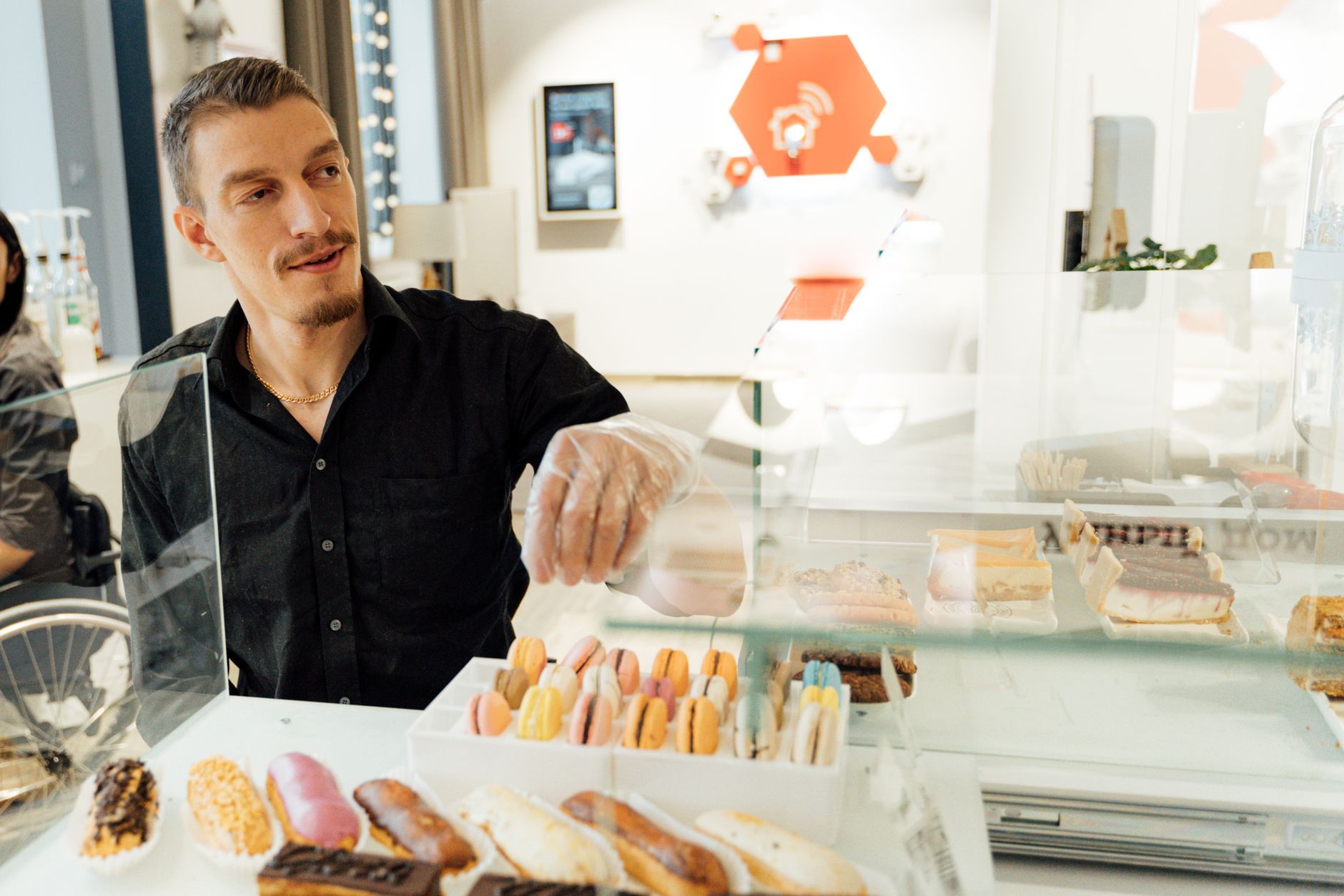 Vitrine de pâtisseries : éclairs glacés, macarons colorés et gâteaux dans un café lumineux.